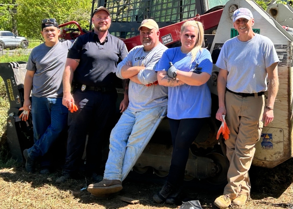 FCPD officers and administrative staff lean against a piece of equipment to pose for a picture during one of their FCPD Works projects.